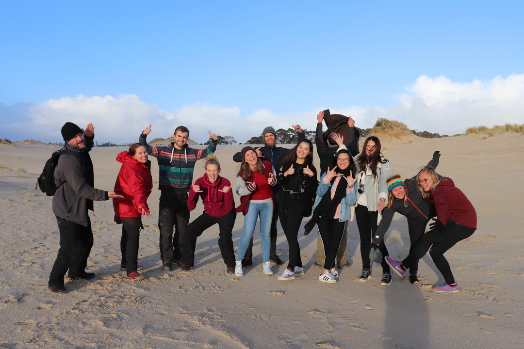 Groupe de personnes posant sur une plage de sable avec un ciel dégagé.