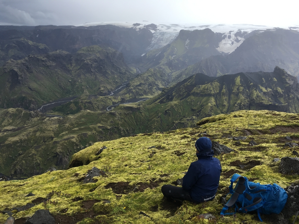 Randonneur assis sur une montagne moussue avec une vue sur une vaste vallée.
