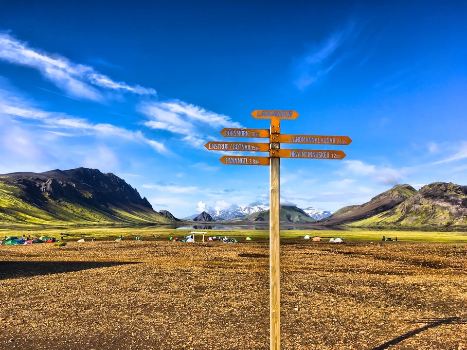 Panneau de signalisation directionnelle avec des montagnes et des tentes en arrière-plan.