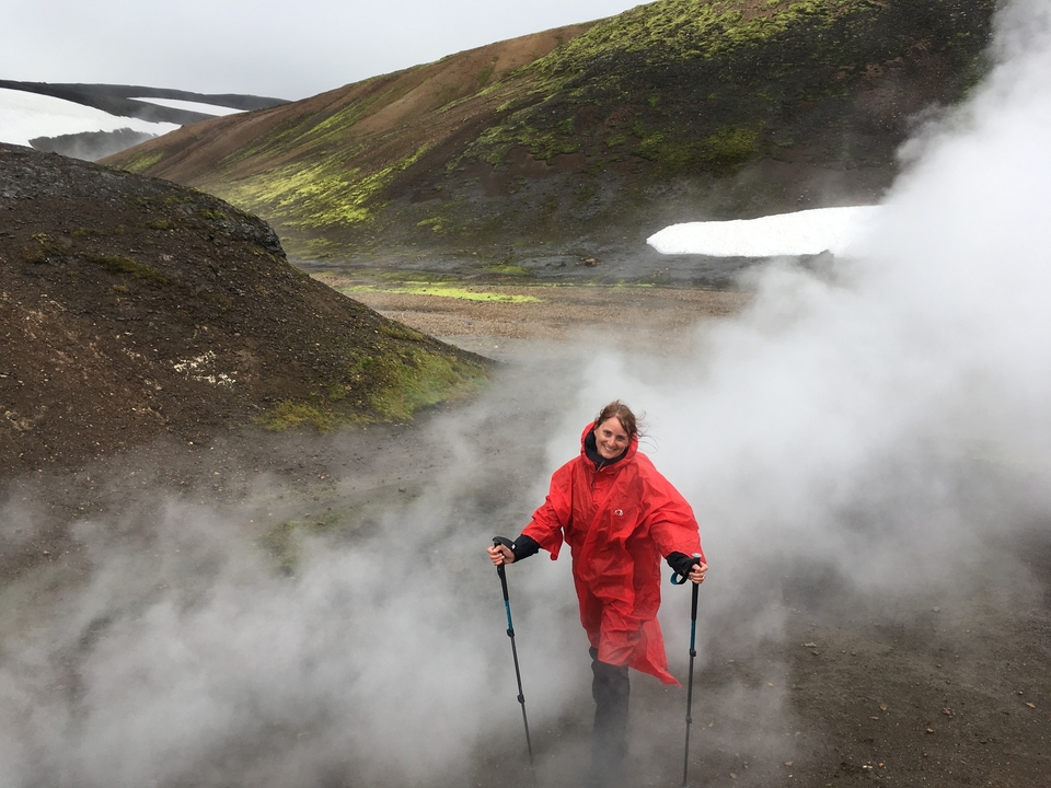 Personne en imperméable rouge faisant de la randonnée à travers un paysage volcanique brumeux.