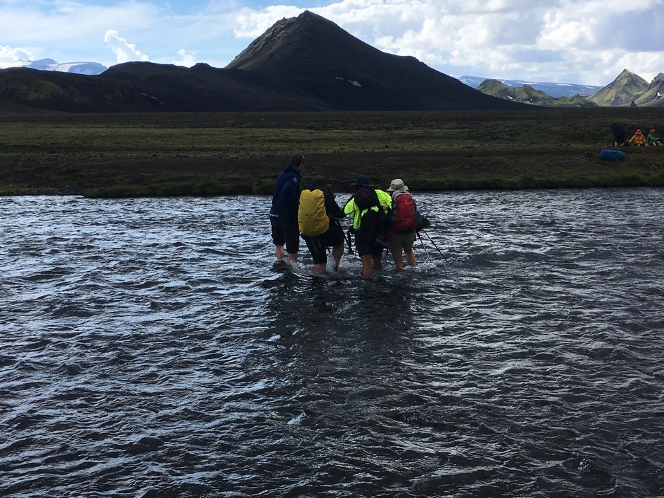 Des gens traversant une rivière avec des bâtons de randonnée.