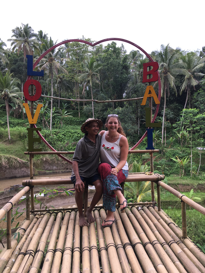 Two people sitting on a bamboo structure in a lush area.