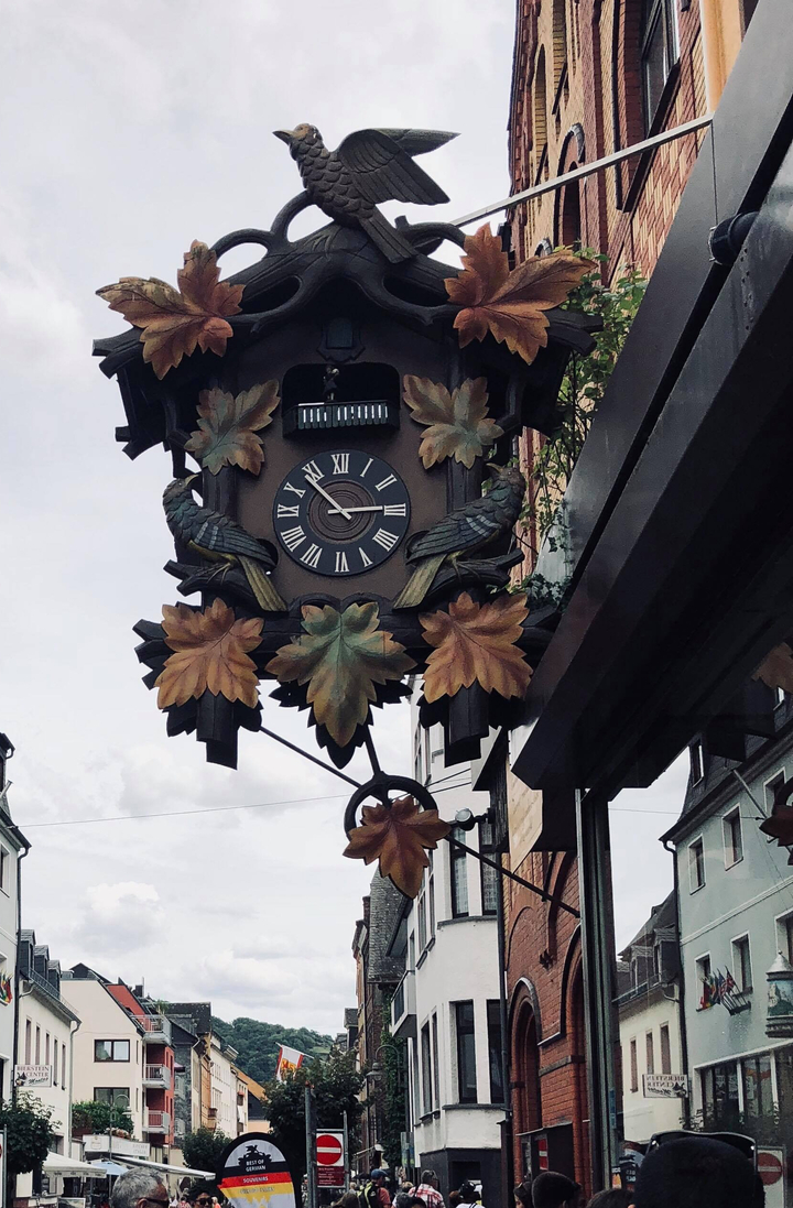 Horloge décorative avec motifs de feuilles et d'oiseaux dans un cadre de rue.