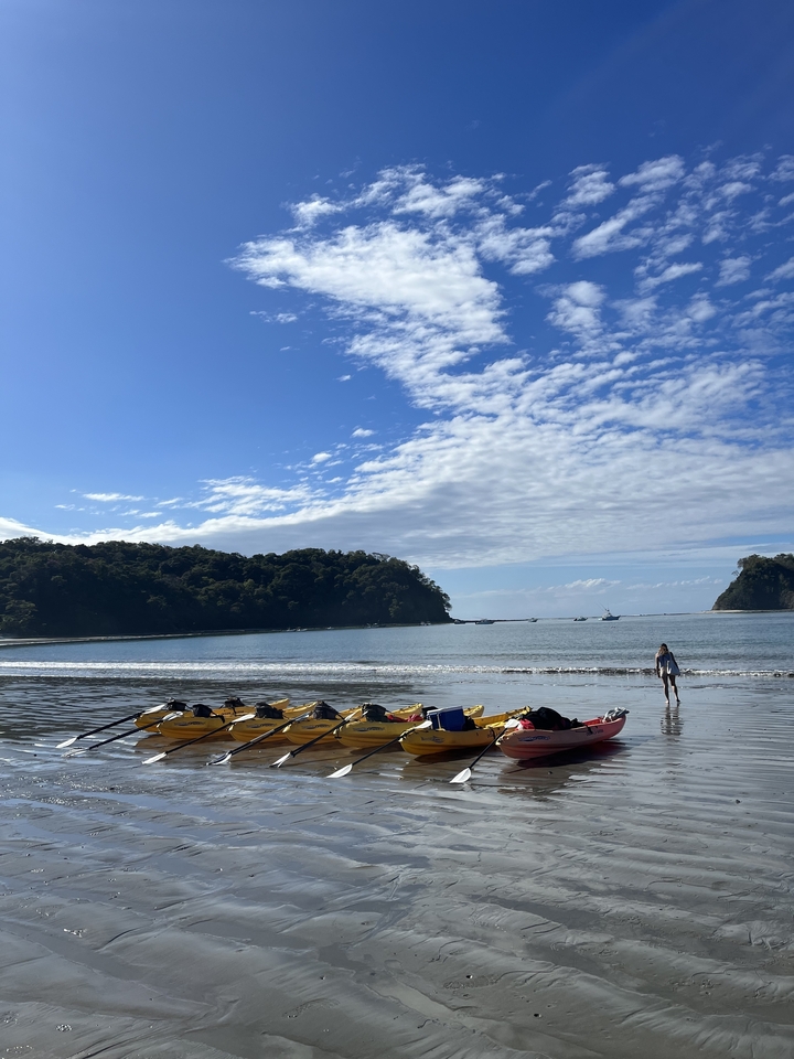 Plage avec des kayaks et une personne qui marche près du rivage.