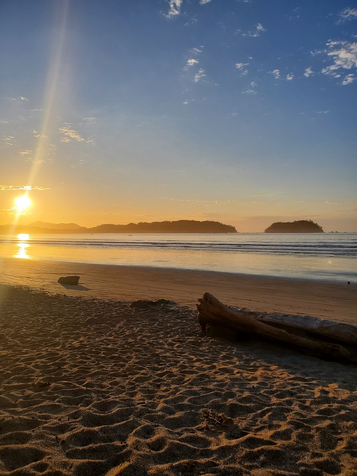 Coucher de soleil sur une plage avec des îles au loin.