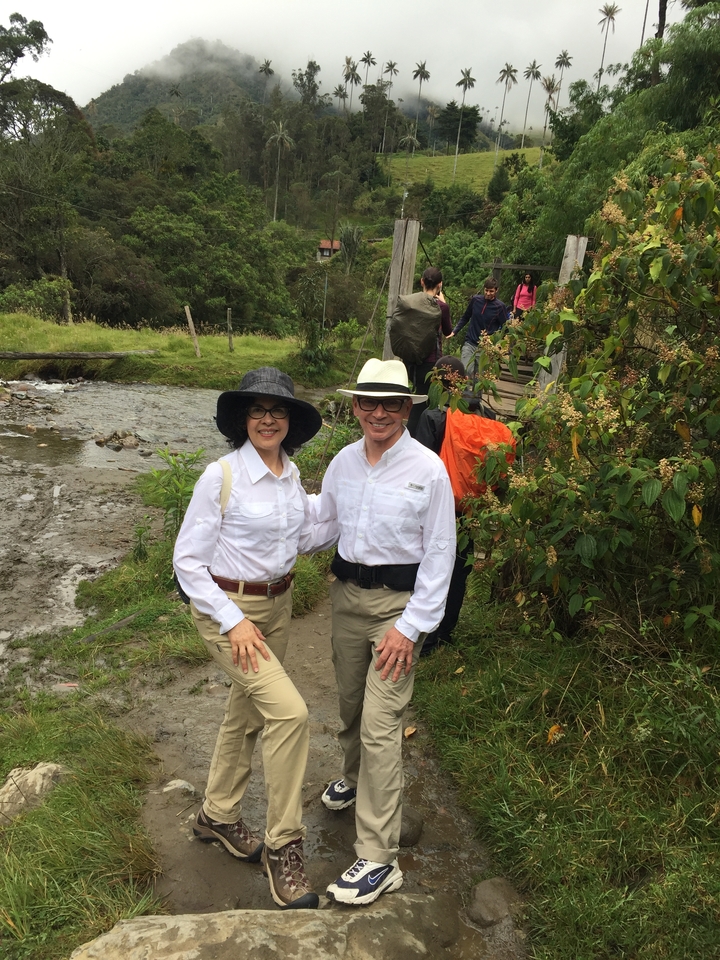 Un couple posant près d'un ruisseau et d'un pont en bois dans un cadre naturel.