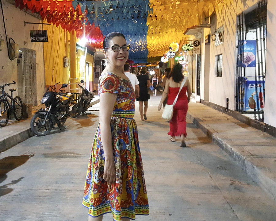 Une femme dans une robe colorée debout dans une rue éclairée.