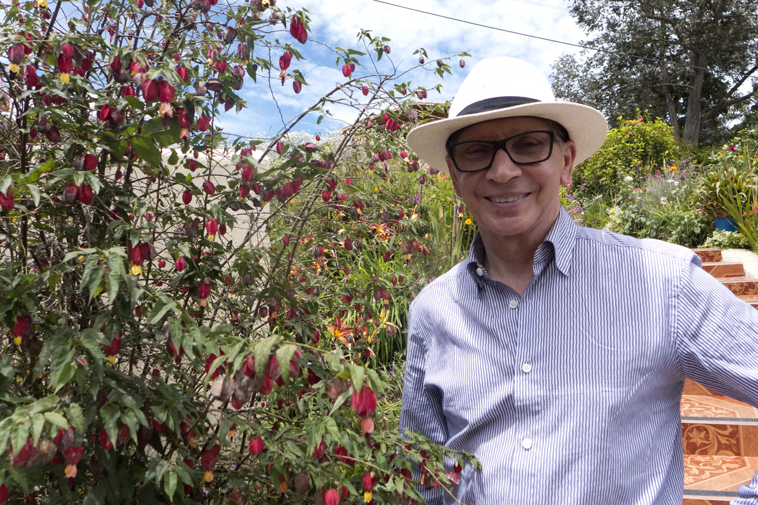 Un homme portant un chapeau debout près de plantes avec des fleurs rouges.