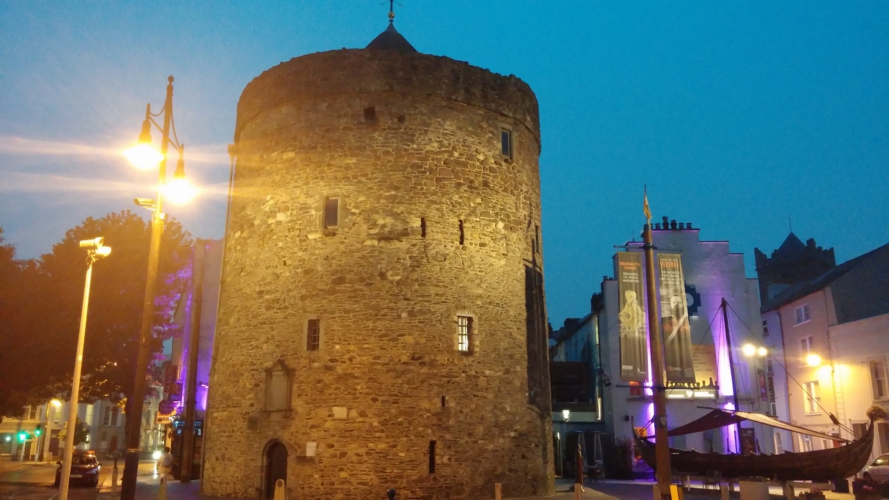 Une tour ronde historique illuminée au crépuscule dans un centre-ville.