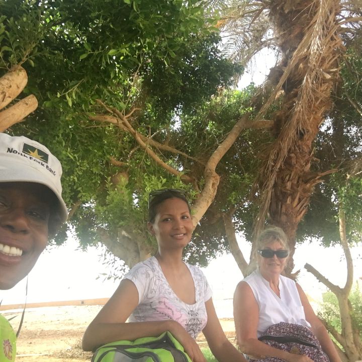 Trois personnes assises sous des arbres, souriant à la caméra.