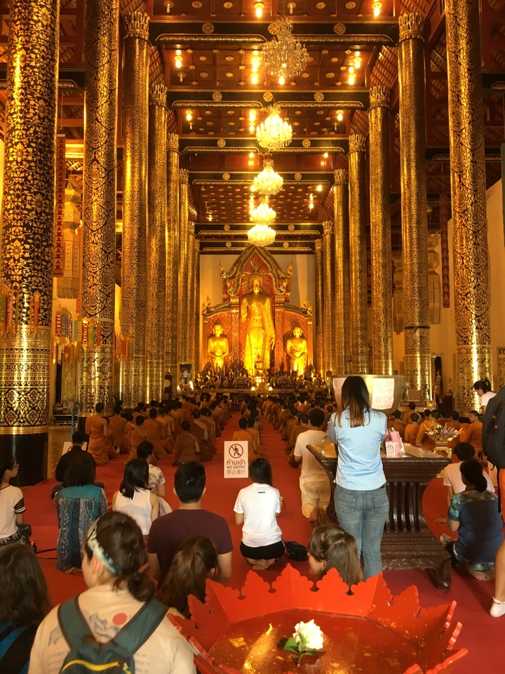 À l'intérieur d'un grand temple avec des décorations dorées et des moines assis.