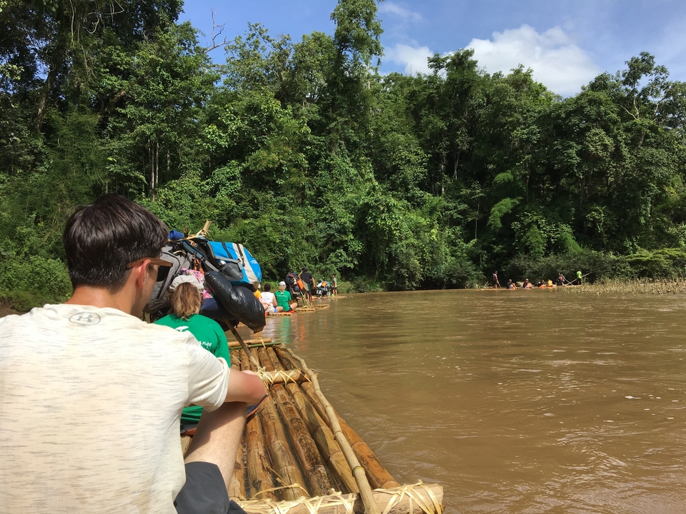 Des gens font du rafting sur une rivière boueuse entourée d'une forêt dense.