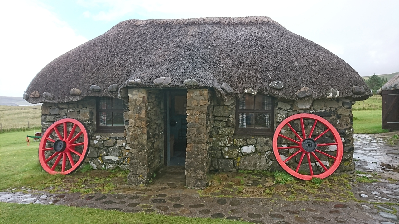 A rustic stone cottage with a thatched roof and wheel decorations.