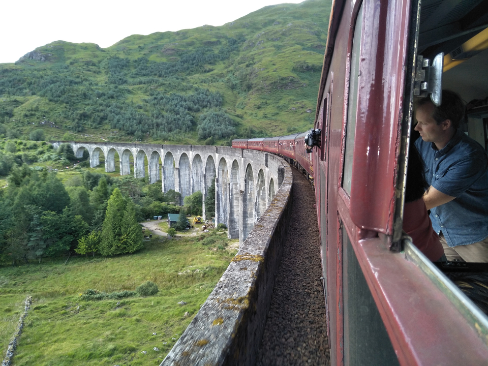 Un train traversant un viaduc célèbre avec un paysage montagneux en arrière-plan.