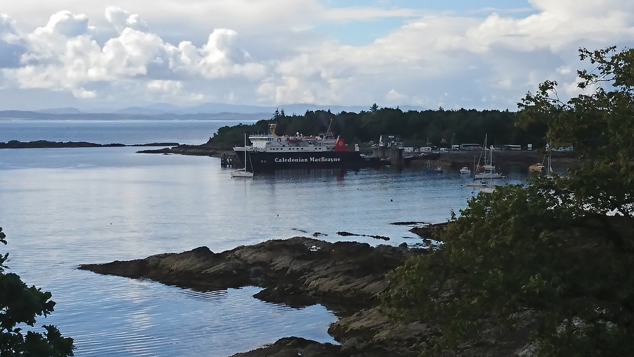Un ferry accosté au rivage avec des eaux calmes et des collines au loin.