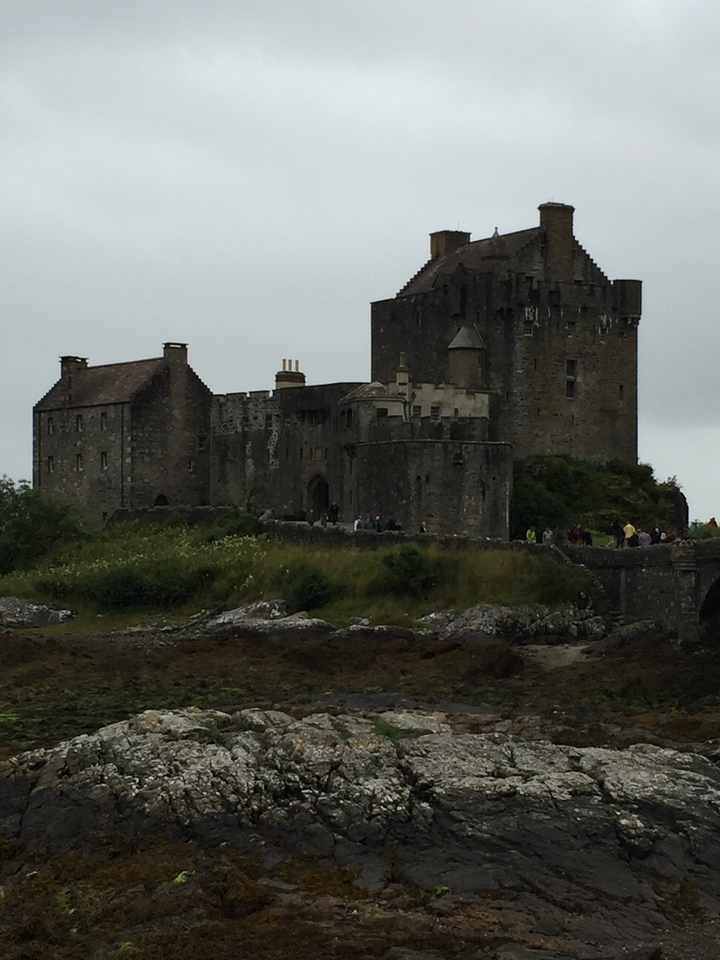 Château médiéval sur un paysage herbeux avec des touristes.