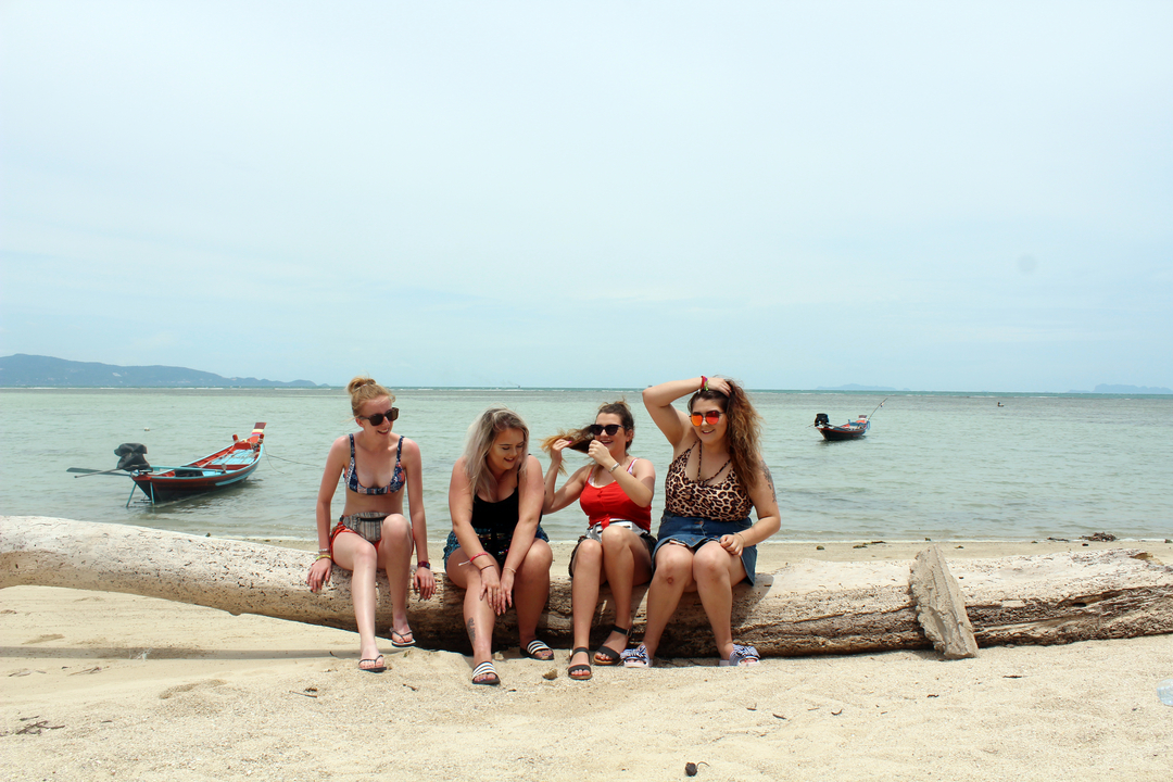 Groupe de personnes assises sur une bûche à une plage avec des bateaux.
