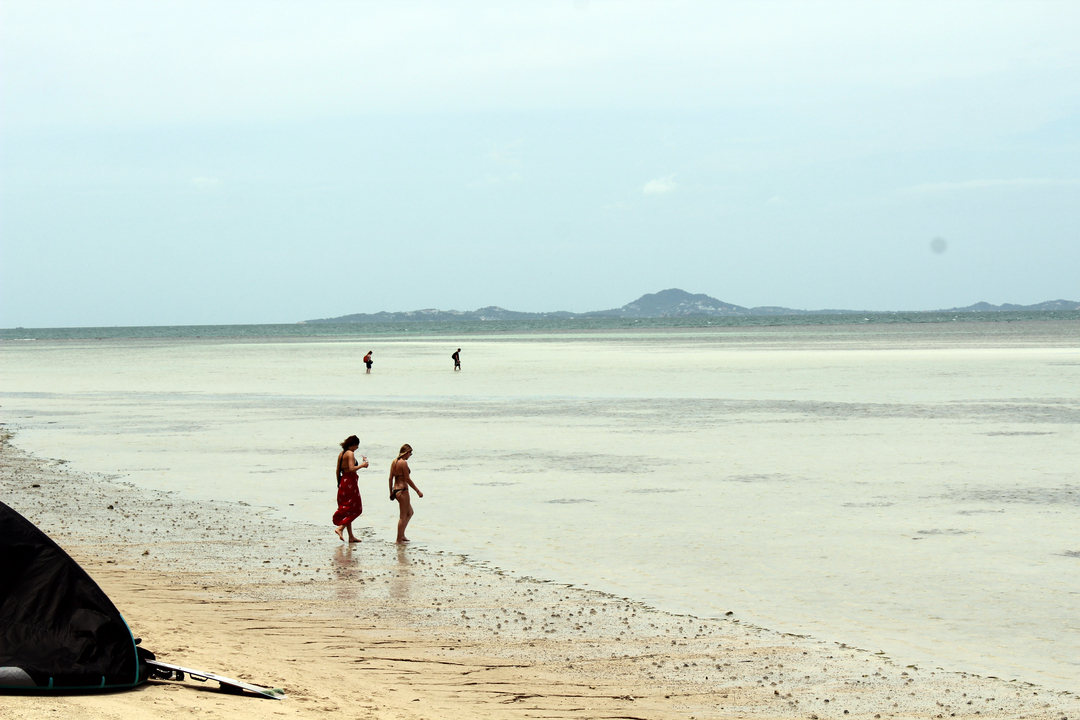 Des gens marchant sur une plage peu profonde avec des montagnes au loin.
