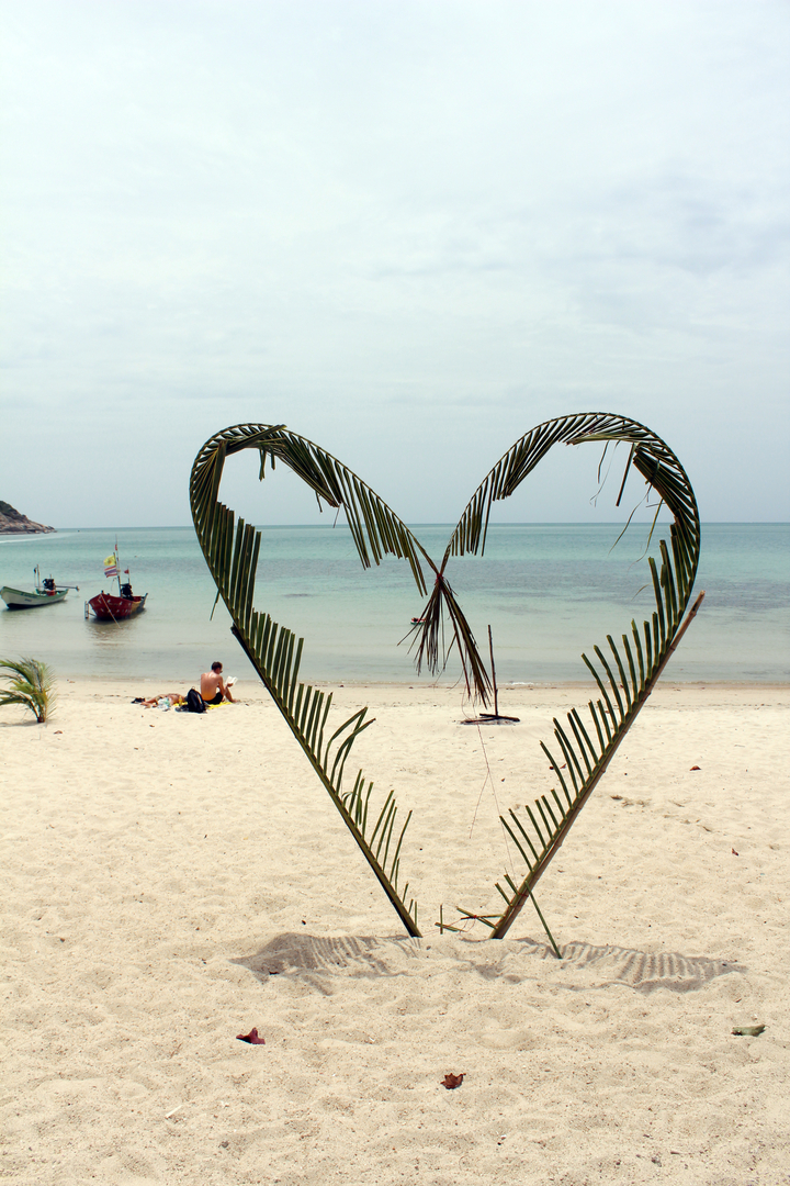 Décoration de feuille de palmier en forme de cœur sur une plage tranquille.
