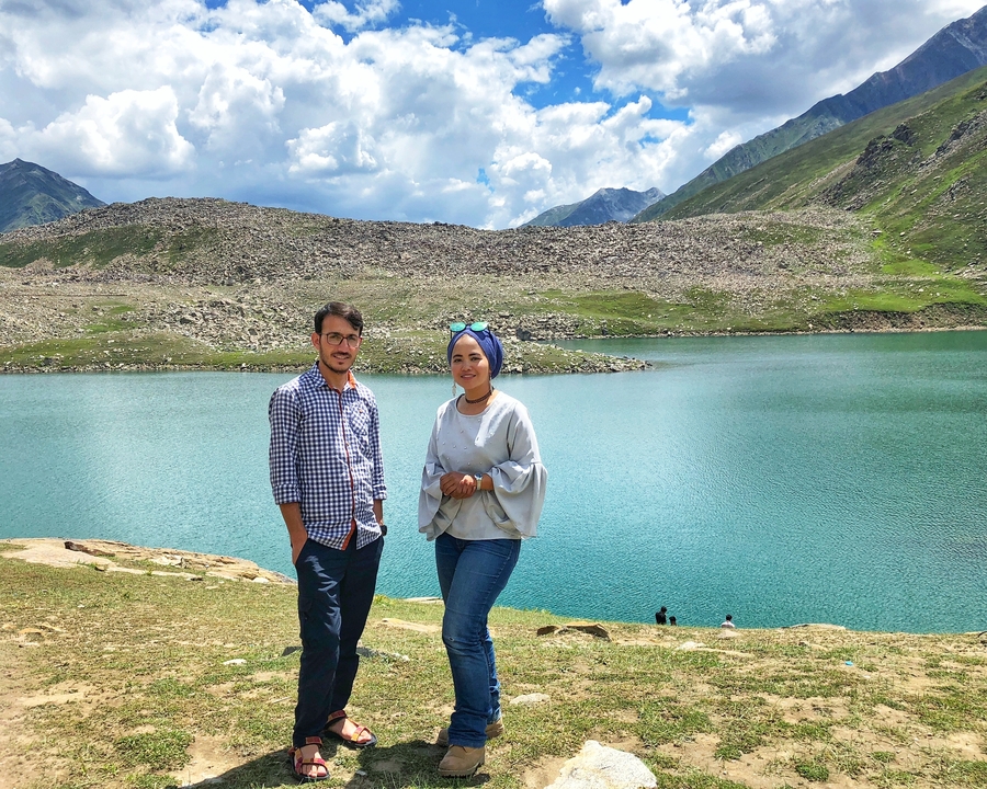 Deux personnes posant devant un lac avec des montagnes en arrière-plan.
