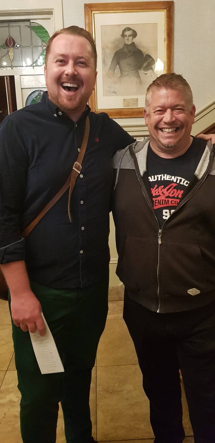 Deux hommes souriants posant à l'intérieur.