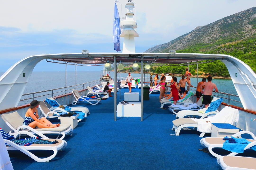 Des gens se prélassant sur le pont d'un yacht avec des montagnes en arrière-plan.