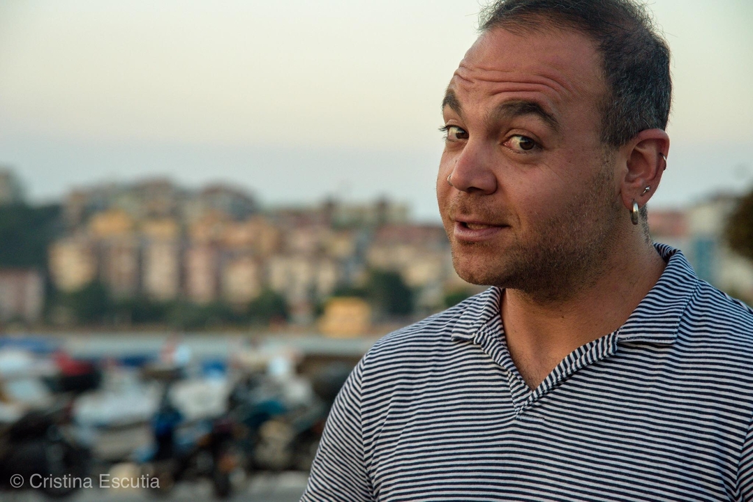 Personne avec une boucle d'oreille et une chemise rayée devant des bâtiments flous.