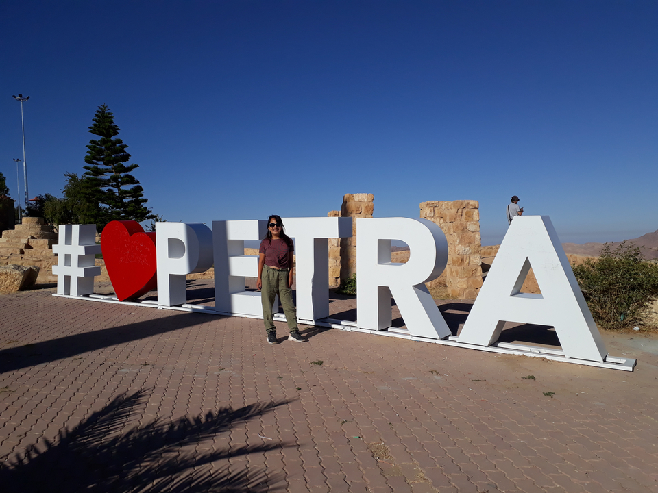 Personne posant à côté d'un grand panneau de Pétra.