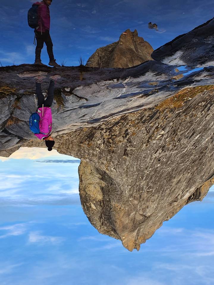 Personne debout à côté d'une grande formation rocheuse sur une montagne.
