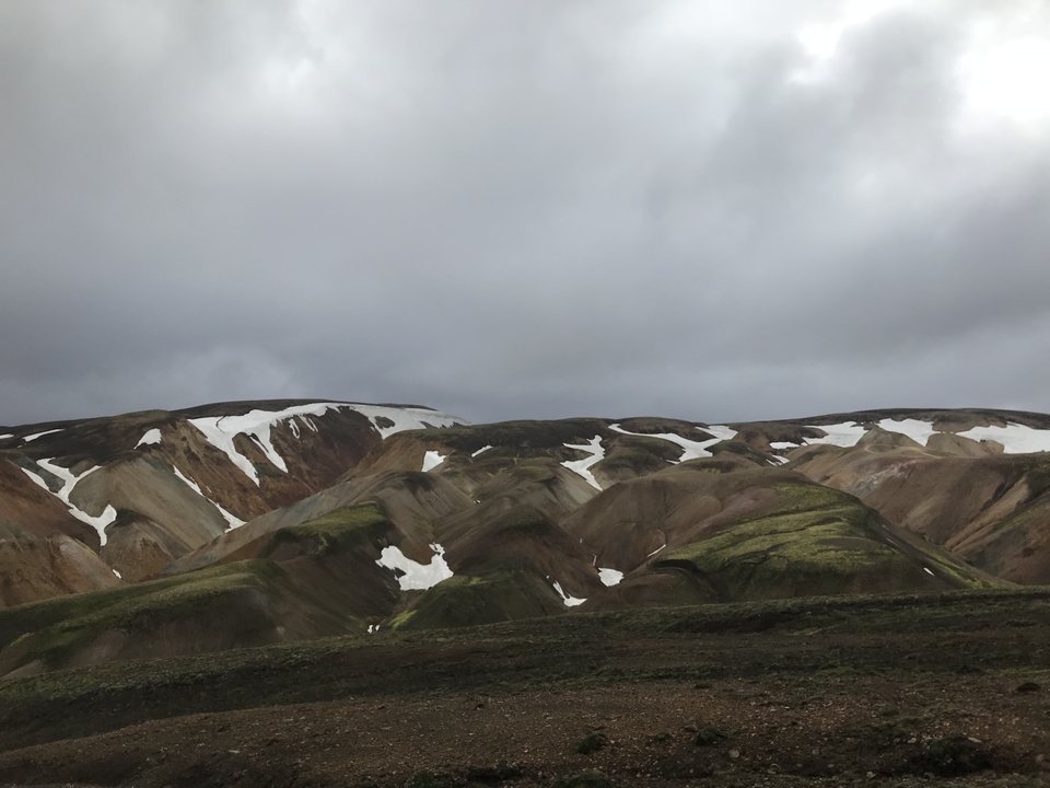 Montagnes colorées avec des plaques de neige sous un ciel nuageux.