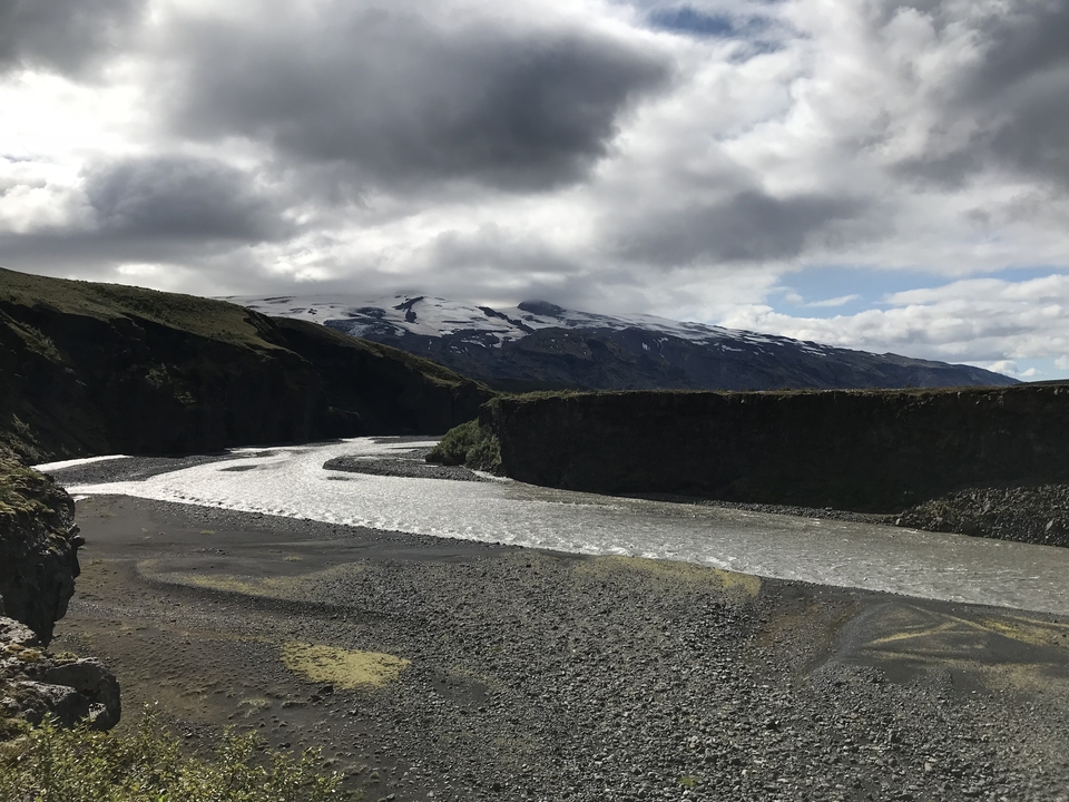 Rivière coulant à travers un paysage rocheux avec des montagnes enneigées au loin.