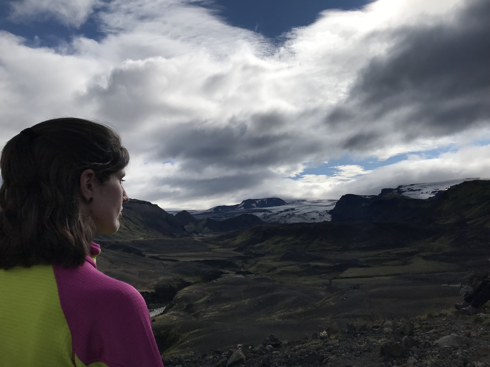 Femme regardant un paysage pittoresque avec des montagnes et un ciel partiellement nuageux.