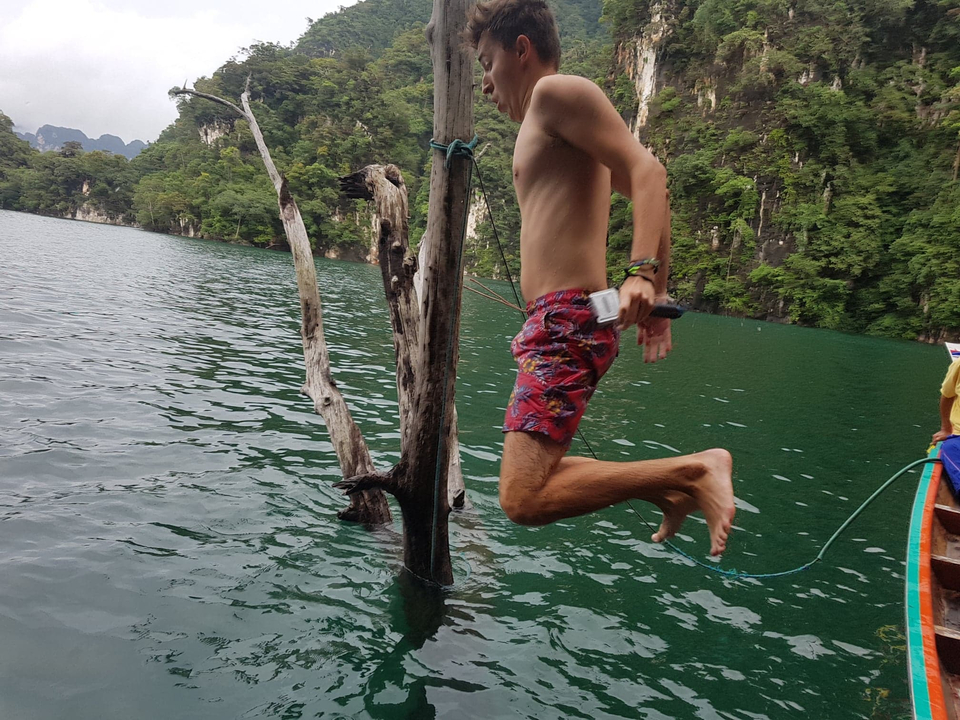 Person jumping into a lake from a boat surrounded by cliffs.