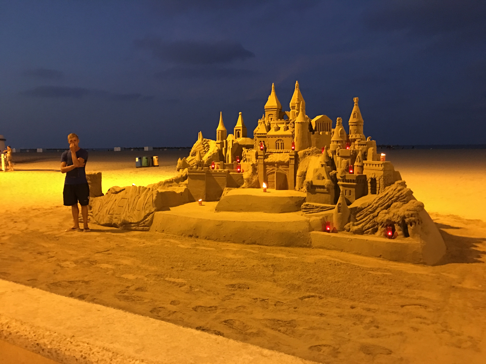 Château de sable élaboré sur une plage au crépuscule avec une personne à proximité.