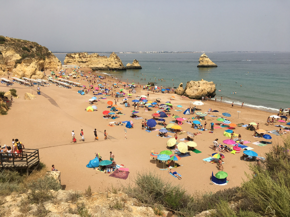 Plage bondée avec des parasols colorés et des formations rocheuses.
