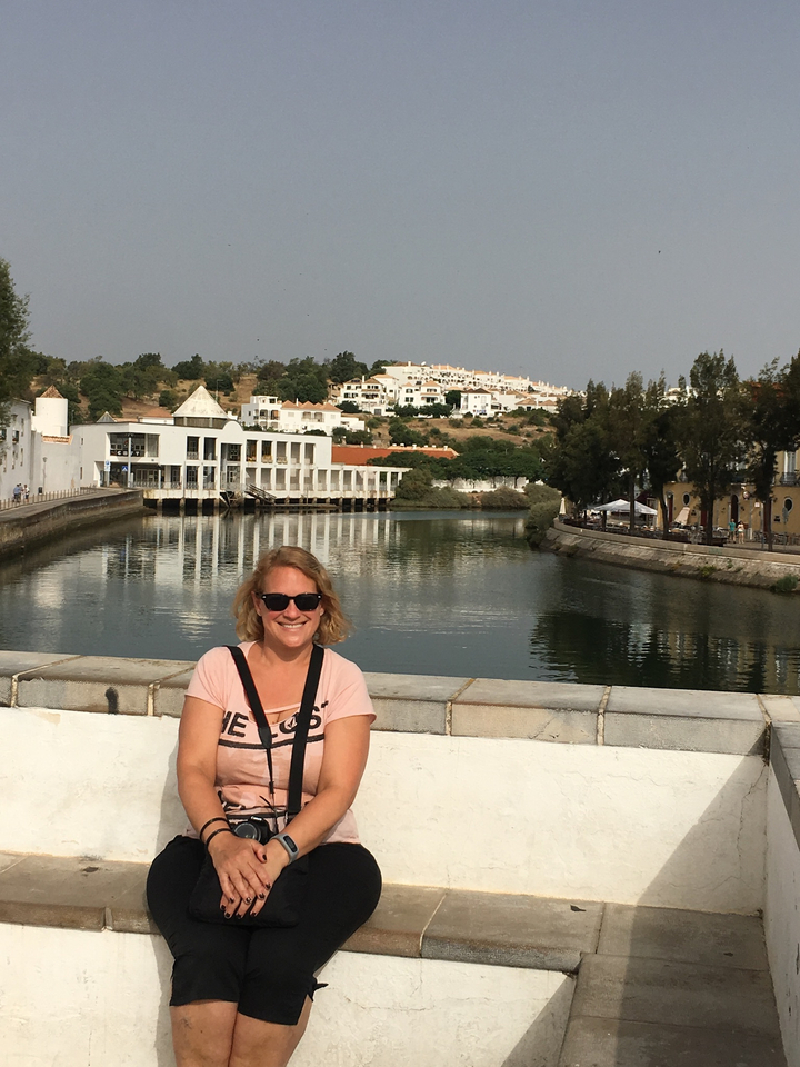 Femme assise au bord d'un canal avec des bâtiments blancs et des arbres.