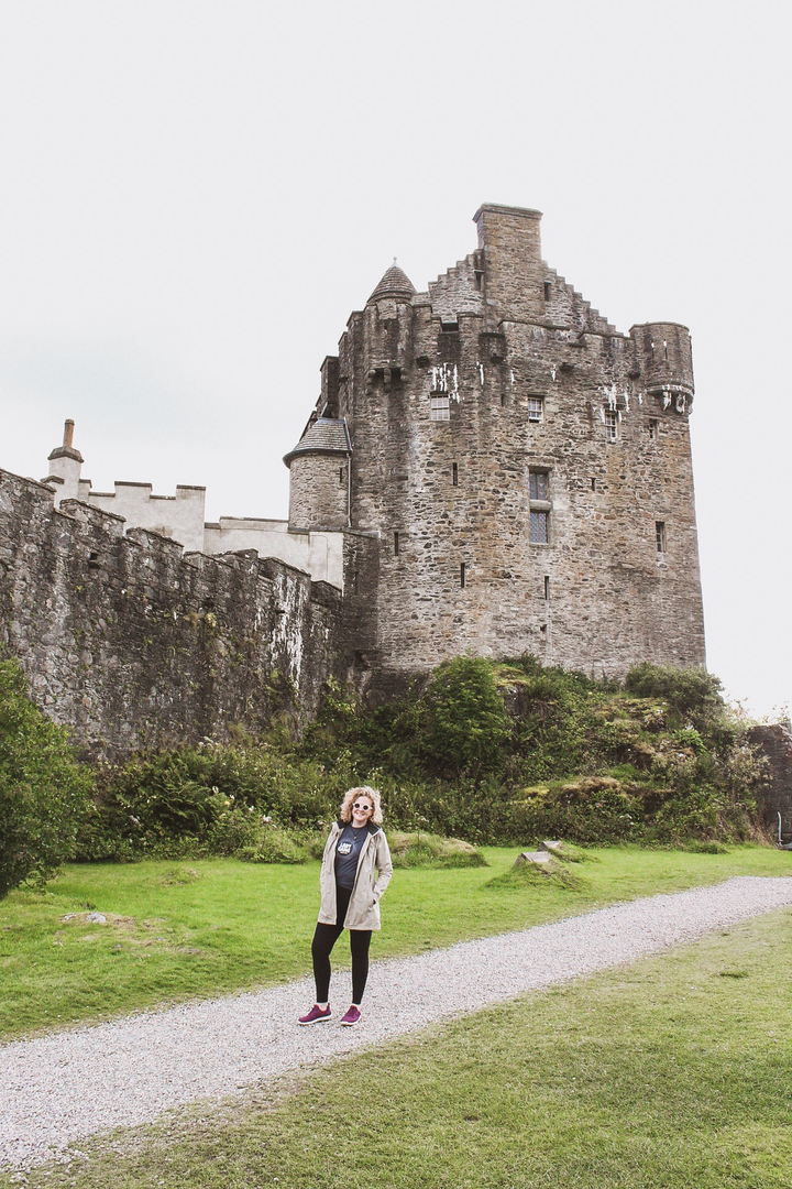 Femme debout devant un grand château de pierre.