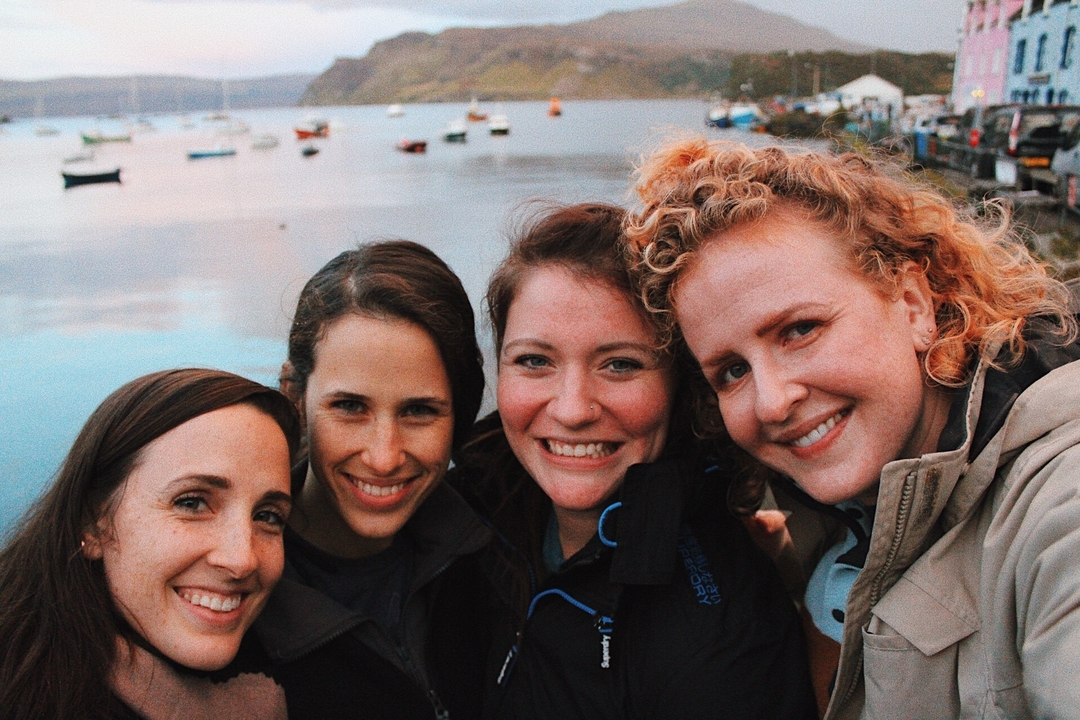 Quatre amis posant avec un décor d'eau pittoresque en arrière-plan.