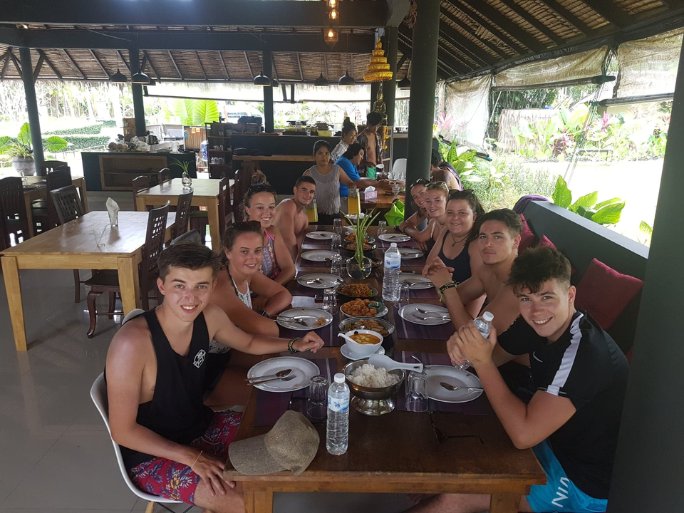 Group sitting together at a table with plates and food in a sheltered outdoor area.