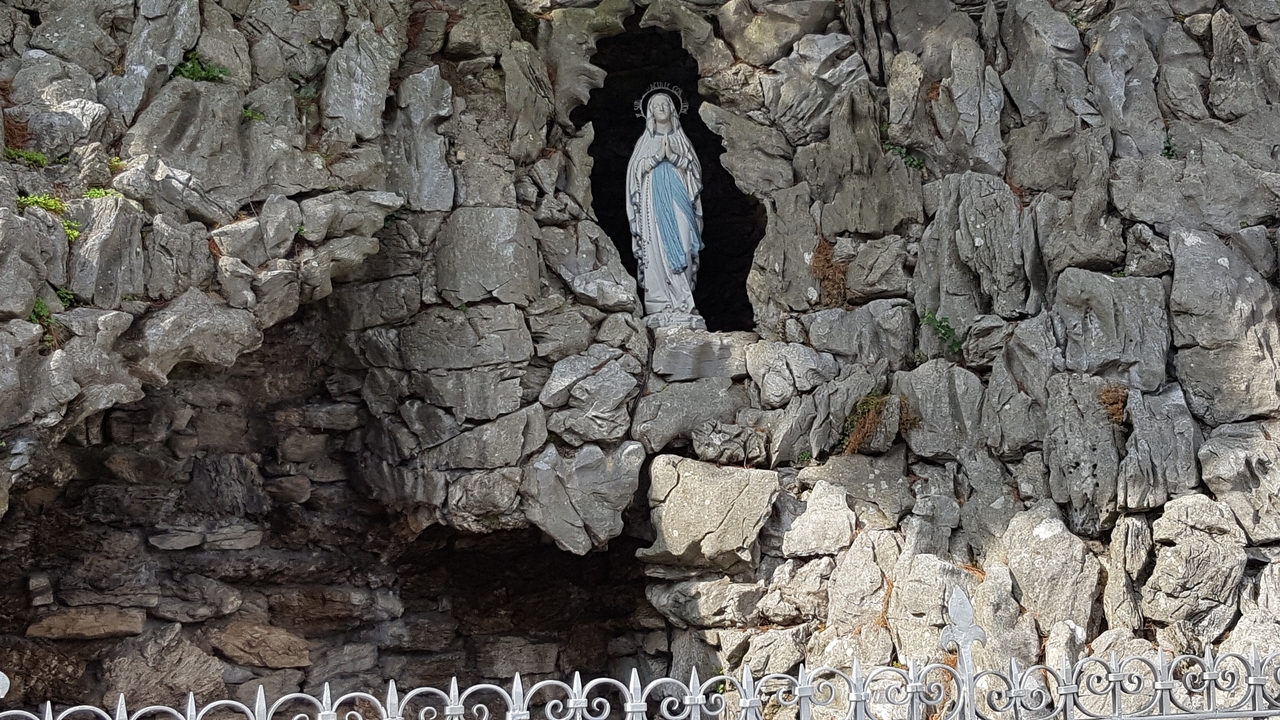 Statue d'une figure religieuse située dans une grotte rocheuse.