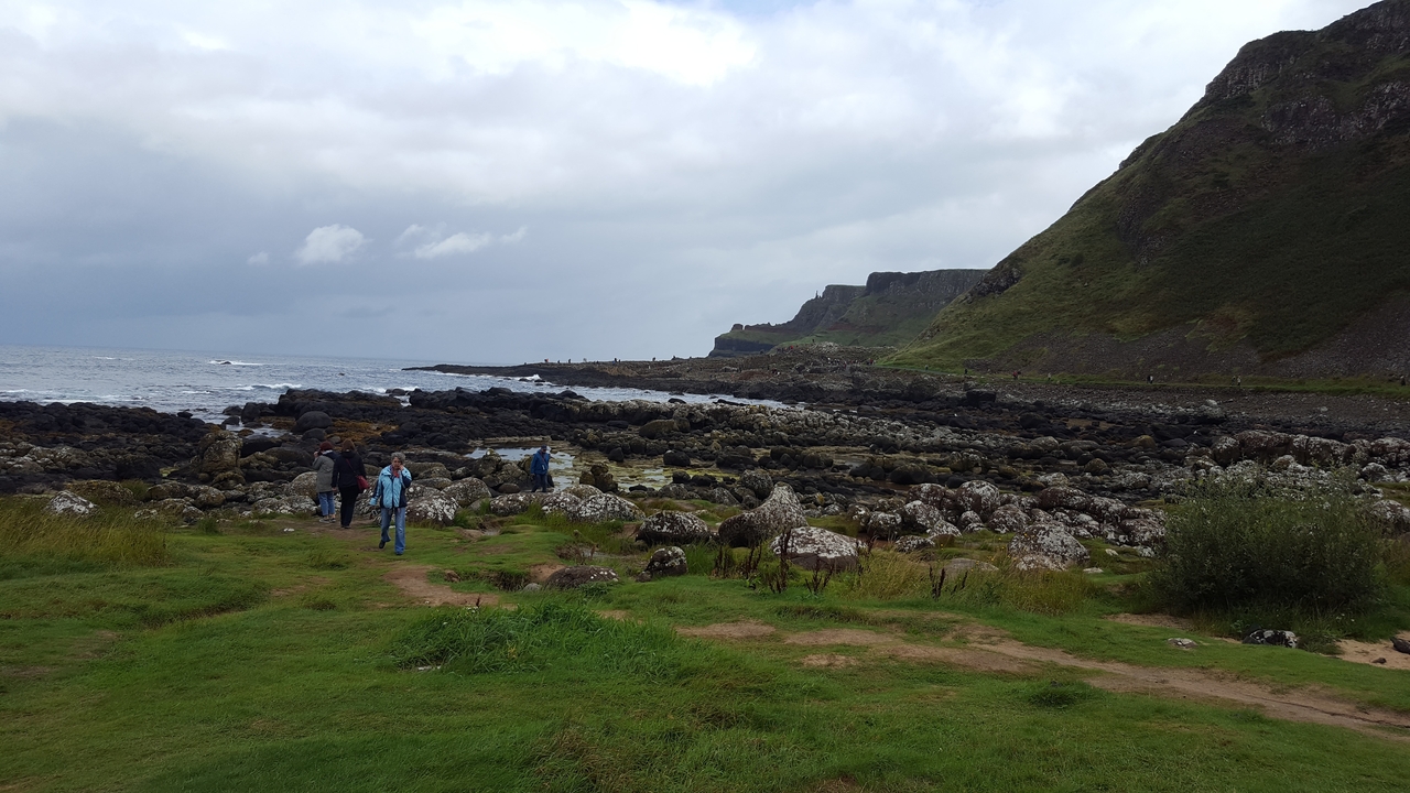 Paysage côtier rocheux avec des collines vertes et un ciel nuageux.
