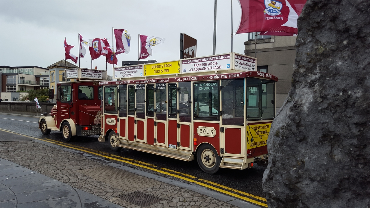 Tramway touristique avec drapeaux et panneaux d'information garé dans une ville.