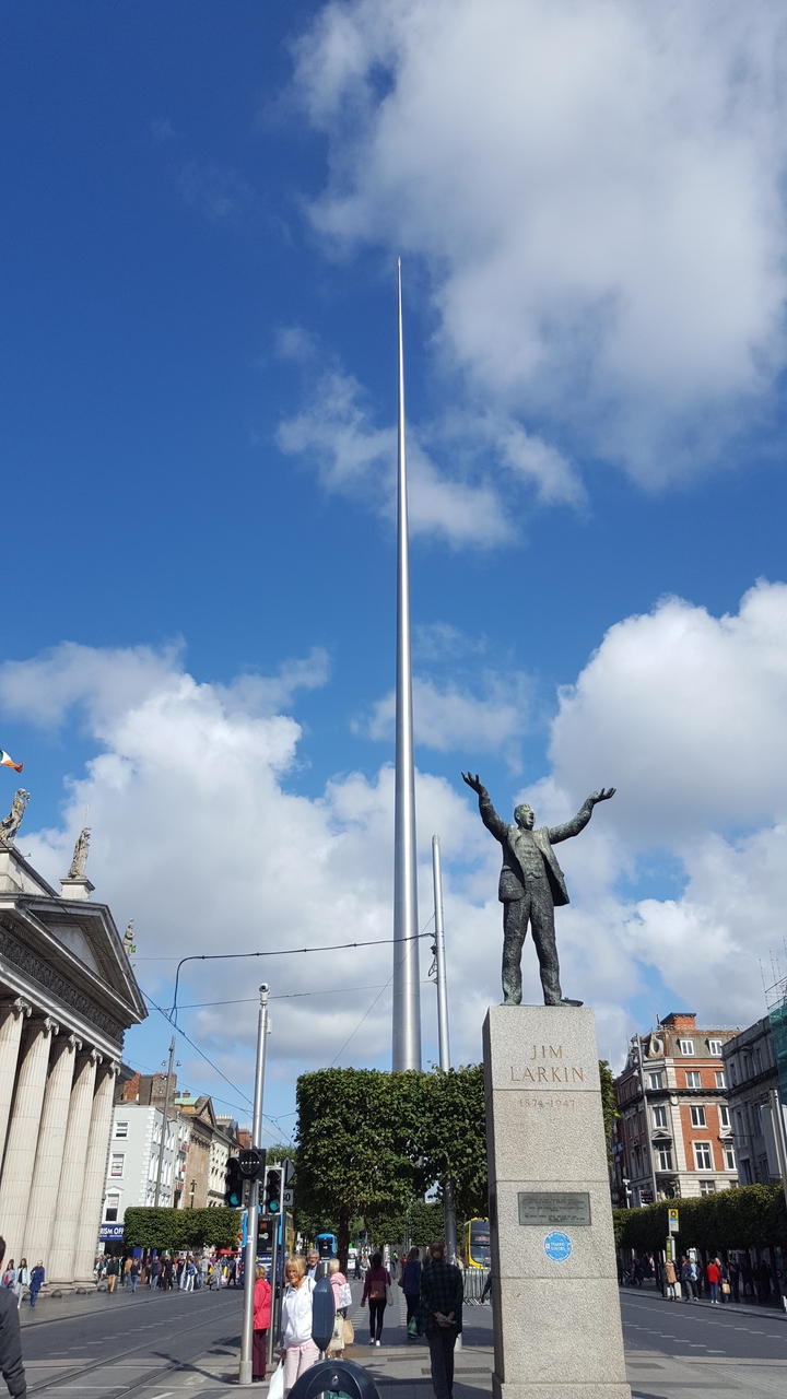 Statue d'un homme aux bras étendus à côté d'une haute flèche.