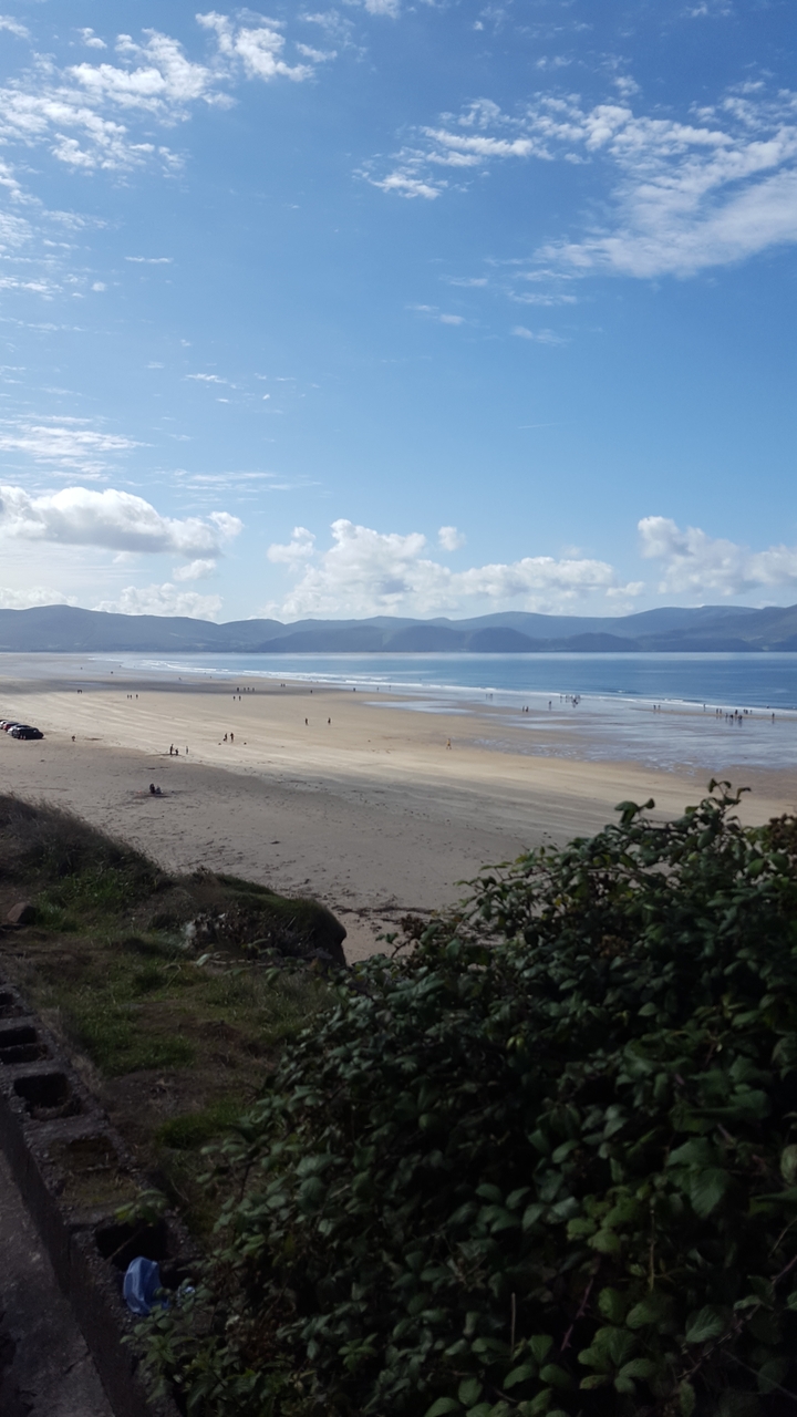 Large plage de sable avec des gens au loin et un arrière-plan montagneux.