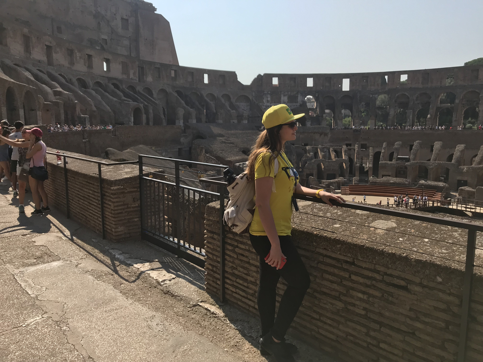 Personne avec un chapeau jaune posant à l'intérieur d'un colisée historique.