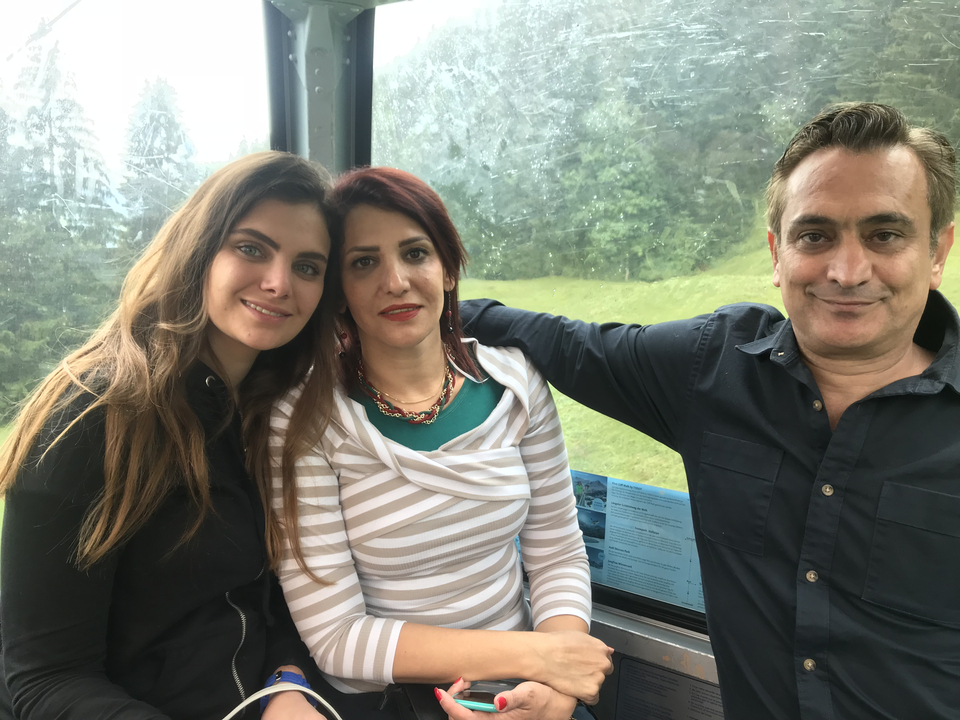 Trois personnes assises à l'intérieur d'une gondole ou cabine avec une vue sur les arbres à l'extérieur.