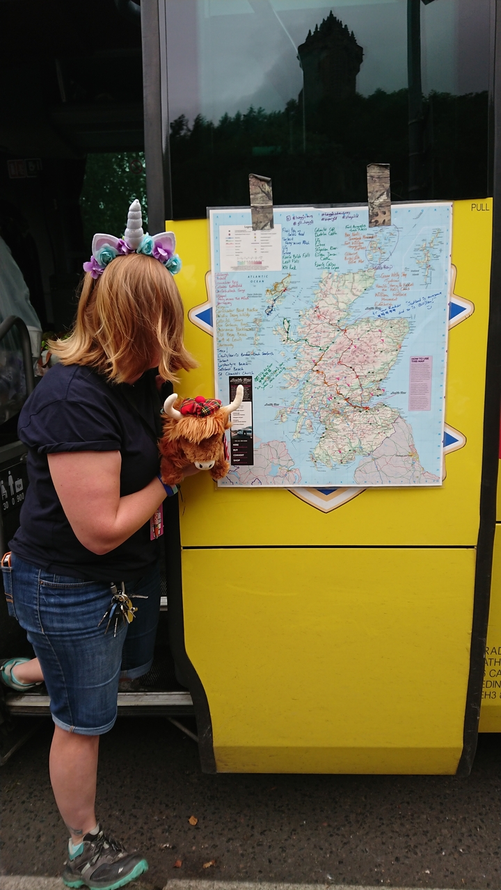 Person holding a stuffed animal next to a map of Scotland.