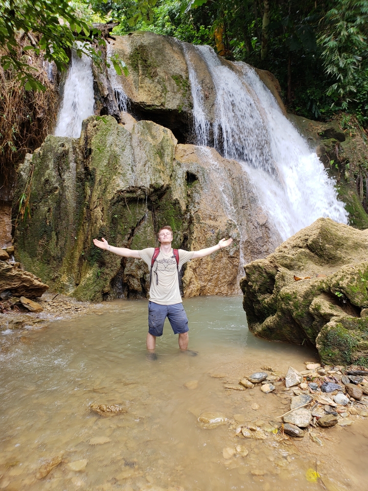Person posing in front of a waterfall with arms open.