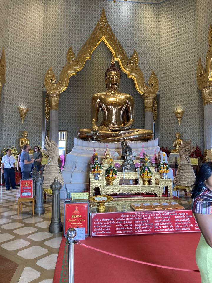 Statue dorée de Bouddha à l'intérieur d'un temple avec des personnes qui observent.