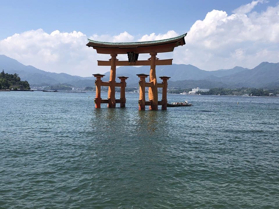 Célèbre porte torii se dressant dans l'eau avec des montagnes en arrière-plan.